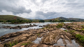 Rocas erosionadas en primer plano, un río que fluye, vegetación en las orillas, colinas verdes al fondo y cielo con nubes.