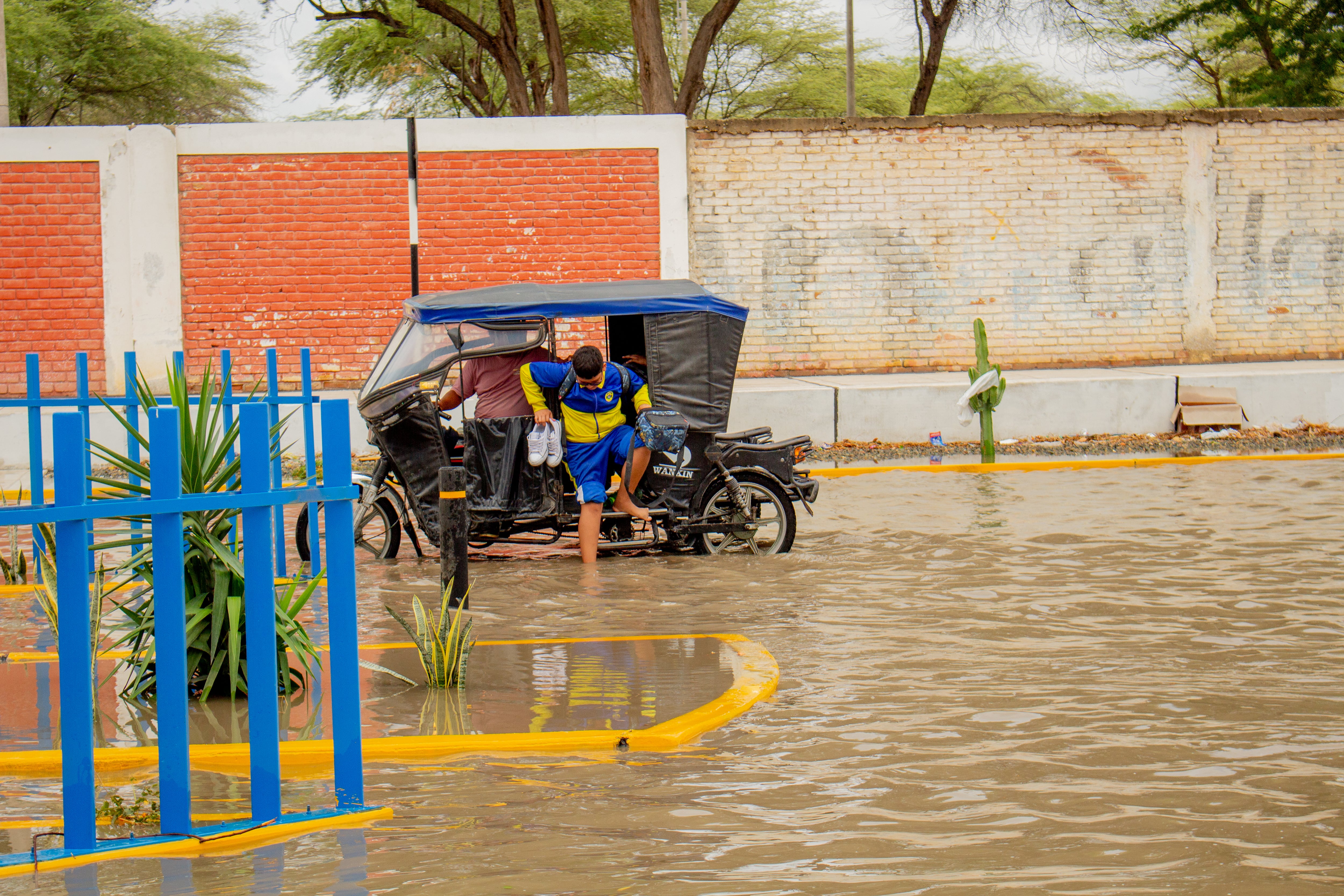 Un estudiante descalzo desciende de un mototaxi en una calle inundada por las lluvias en Piura, donde el agua dificulta el tránsito peatonal y vehicular. (UNICEF)