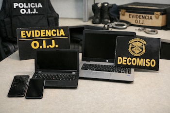 Cuatro dispositivos electrónicos, incluyendo dos laptops y dos celulares, junto a carteles de "EVIDENCIA O.I.J." y "DECOMISO" sobre una mesa.