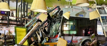 Vista interior de un autobús gris que ha atravesado la vitrina de una tienda, con cristales rotos, escombros, estanterías de vino y lámparas de techo caídas