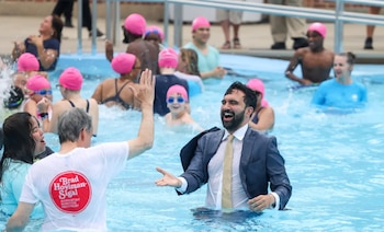 Un grupo de personas en una piscina. Un hombre con traje de calle mojado y corbata. Otro hombre con camiseta blanca. Varios llevan gorros rosados