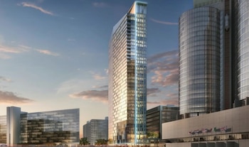 Visualización de un rascacielos de vidrio con edificios anexos, varias banderas y un cielo con nubes al atardecer o amanecer