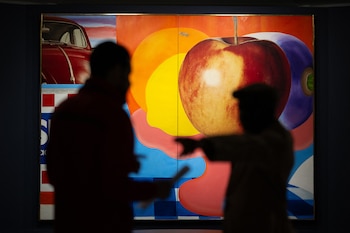 Siluetas de dos personas frente a un cuadro colorido con una manzana grande, un auto rojo y formas geométricas