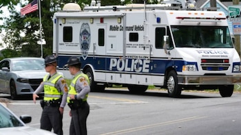 Dos oficiales de policía con chalecos de alta visibilidad de frente a un vehículo de comando móvil de la policía de Winston-Salem, con una bandera estadounidense al fondo