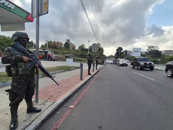 Un soldado uniformado con fusil de asalto permanece de pie en una acera cerca de una calle con automóviles en circulación