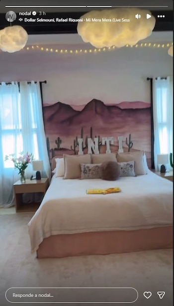 Vista frontal de un dormitorio con una cama grande y colchón blanco, dos mesitas de noche con lámparas y un mural de montañas y cactus con el nombre INTI en la pared trasera