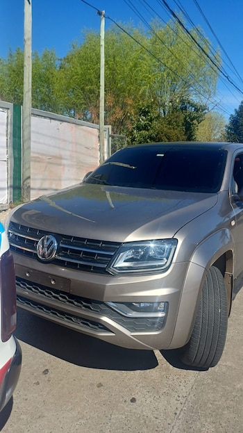 Una camioneta de color marrón metalizado estacionada en la calle junto a postes de madera y vegetación bajo un cielo despejado