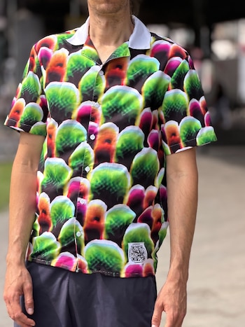 Torso de un hombre con camisa de manga corta estampada en verde, rosa y naranja, y un parche con código QR en la parte inferior