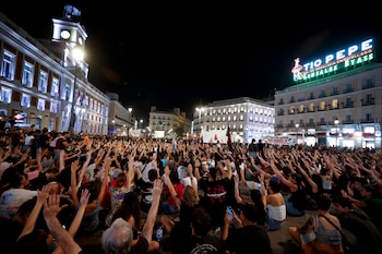 Una multitud de personas sentadas en una plaza urbana de noche alza sus manos hacia el centro