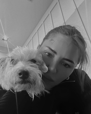 Fotografía en blanco y negro de Cande Tinelli inclinada junto a un perro pequeño de pelaje claro
