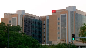 Vista exterior del Jennie Sealy Hospital en Texas, un edificio moderno de varios pisos con fachadas de color beige y vidrio, rodeado de árboles verdes