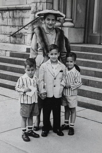 Fotografía en blanco y negro de una mujer con sombrero y estola junto a tres niños en las escaleras exteriores de un edificio de piedra