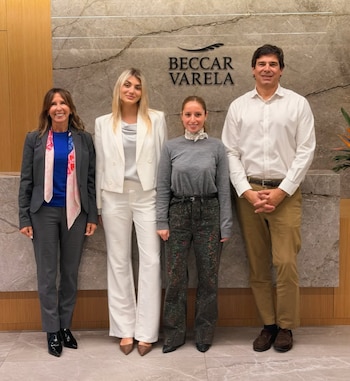 Cuatro personas con vestimenta formal posan frente a una pared de mármol que exhibe el nombre Beccar Varela