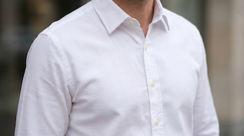 Primer plano de la parte superior del torso de un hombre vistiendo una camisa blanca de manga larga. Se aprecian el cuello, la solapa de botones y la tela texturizada.