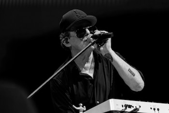 Un primer plano en blanco y negro de Andrés Calamaro cantando en el escenario, con gorra, gafas de sol y un micrófono en mano