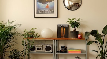 Primer plano de una estantería con macetas, libros, un radiocasete plateado, una cámara Polaroid y un póster de "Le Château dans le Ciel".