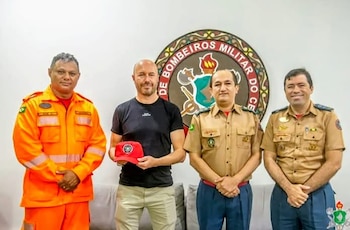 Cuatro hombres posan sonriendo frente a un emblema circular. Tres visten uniformes, uno naranja y dos caqui, mientras el cuarto, Diego, sostiene una gorra roja