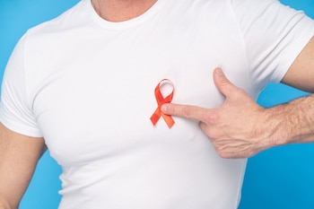 Torso de un hombre con camiseta blanca que apunta con el dedo hacia un lazo ubicado sobre su pecho, frente a un fondo azul claro