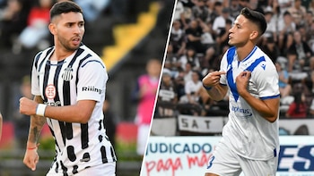 Dos jugadores de fútbol con camisetas de diferentes equipos, uno con uniforme blanco y negro, otro con camiseta blanca y azul, en un estadio con público