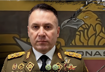 Oficial militar con uniforme de gala de color verde oliva y medallas en el pecho, sobre un fondo con la imagen de un águila