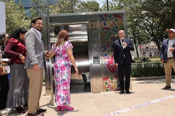Grupo de personas en un evento al aire libre junto a un módulo de baño público inteligente de metal, con una decoración colorida de flores y animales