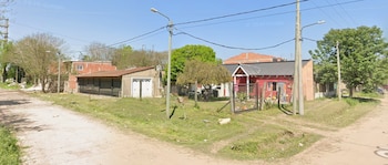 Casas con rejas y alambrados, postes de luz con cables y árboles junto a una calle de tierra bajo un cielo despejado