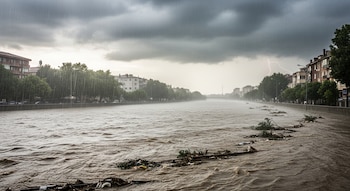 Vista de un río desbordado por lluvias intensas, con árboles y escombros flotando, un rayo en el cielo oscuro y edificios urbanos en las orillas.