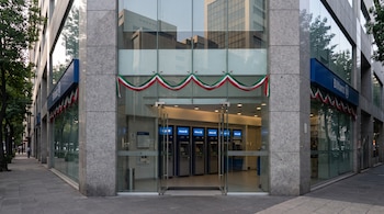 Fachada de esquina de un edificio de cristal con cajeros automáticos en el interior y guirnaldas tricolores sobre la entrada.