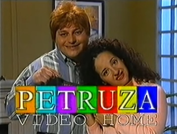 Un hombre de cabello rojizo y una mujer de cabello rizado oscuro sonríen frente al logo multicolor 'PETRUZA VIDEO HOME'