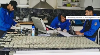 Tres policías cuentan fajos de billetes de cien dólares sobre una mesa oscura. Se ven un portátil, una maleta abierta y objetos de investigación