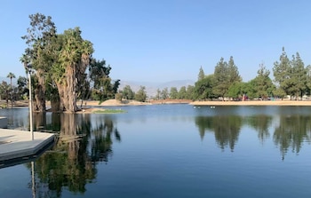 Un lago con árboles de distintas especies en sus orillas e islas, un muelle de concreto en primer plano, un puente de madera al fondo y montañas bajo un cielo despejado