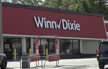 Fachada roja de un supermercado Winn-Dixie con un letrero blanco, una zona de carritos de compras y un vehículo estacionado
