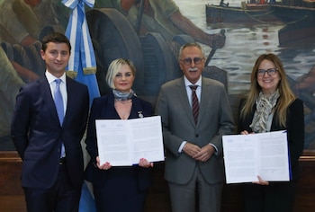 Cuatro personas, dos hombres y dos mujeres, posan sonriendo. Dos mujeres sostienen documentos abiertos. Detrás, una bandera argentina y una pintura mural