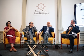 Cuatro panelistas, una mujer y tres hombres, sentados en sillones amarillos durante un evento cultural, con un logo institucional y una pantalla al fondo