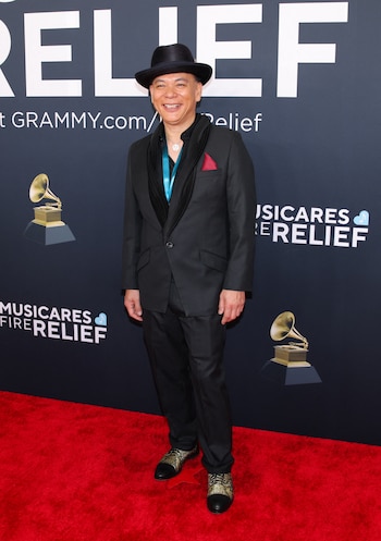 El artista estadounidense Dale Edward Chung eligió un traje negro de corte clásico, acompañado de una camisa negra y un pañuelo rojo que sobresale del bolsillo superior de la chaqueta. Completó el look con una corbata turquesa que aportó un toque de color contrastante y unos zapatos bicolores en negro y verde metálico. Llevó un sombrero negro de ala corta, que añadió un estilo distintivo y casual a su atuendo