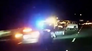 Autopista durante la noche con un automóvil en movimiento frente a vehículos detenidos y luces policiales de emergencia