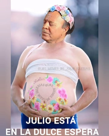 Rostro de Julio Iglesias con corona de flores sobre un cuerpo con barriga pintada de flores y nombres. Manos sostienen el vientre. Texto: JULIO ESTÁ EN LA DULCE ESPERA