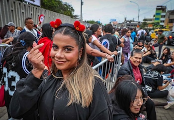 Una mujer sonríe y hace un gesto con la mano frente a una multitud reunida junto a vallas metálicas en la vía pública