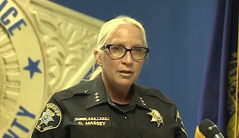 Una agente de policía con uniforme negro, anteojos y una placa con el apellido Massey habla frente a un micrófono