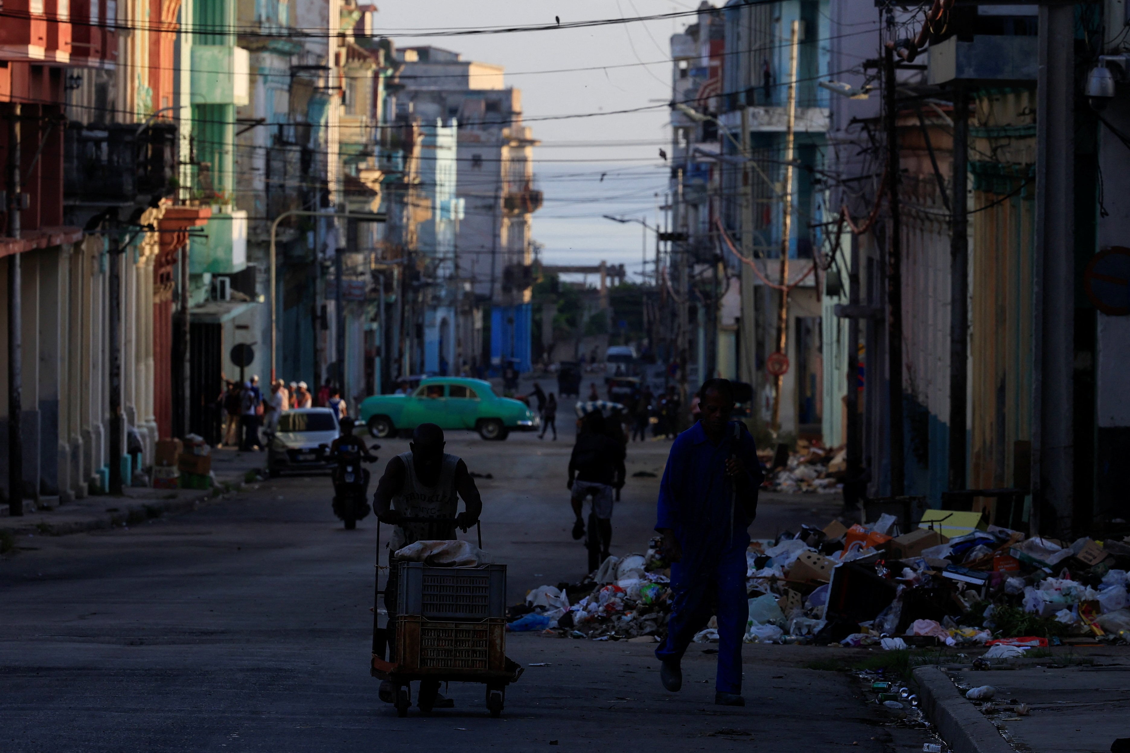 Un hombre empuja una carretilla mientras otro camina cerca por una calle, mientras Cuba lucha por restablecer el suministro eléctrico tras el colapso de su red nacional el día anterior, dejando a millones de personas aún sin electricidad en toda la isla caribeña, en La Habana, Cuba, el 7 de julio de 2026. REUTERS/Norlys Pérez