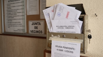 Buzón de metal, una llave, varios sobres, uno dice 'RECLAMACIÓN JUDICIAL - EMBARGO', otros 'URGENTE'. Cartel con 'DEUDA PENDIENTE: 4.500€ + COSTES', tablón de anuncios.