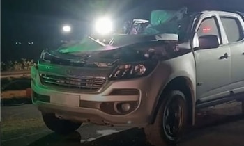 Una camioneta pick up blanca con el capó y el paragolpes delantero visiblemente dañados. Luces de vehículos y ambiente nocturno
