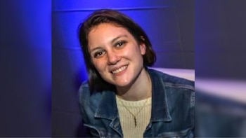 Primer plano de una mujer joven con cabello oscuro corto, ojos marrones, sonriendo ligeramente y vistiendo una chaqueta de mezclilla y un collar