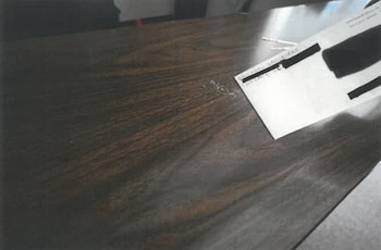 Un sobre blanco con marcas negras que cubren texto y restos de polvo blanco esparcidos sobre una superficie de madera oscura