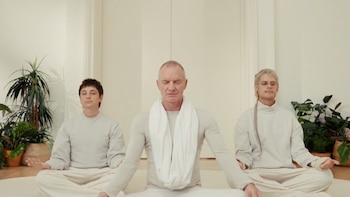 Sting, Ca7riel y Paco Amoroso sentados en el suelo en posición de meditación, con los ojos cerrados y ropa clara, en un cuarto con plantas