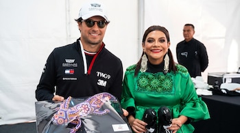 Un hombre con gorra y lentes oscuros sostiene un cuadro con un reptil de cuentas junto a una mujer con vestido verde que porta botas negras.