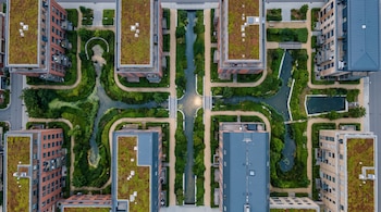 Vista aérea cenital de edificios residenciales con techos verdes, senderos peatonales y canales de agua rodeados de vegetación.