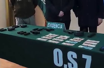 Varias armas de fuego, cargadores y billetes dispuestas sobre una mesa verde con la sigla O.S.7 y un letrero con la palabra EVIDENCIA