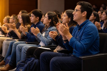 Jóvenes sentados en las butacas de un auditorio sonríen y aplauden dirigiendo su mirada hacia el frente.
