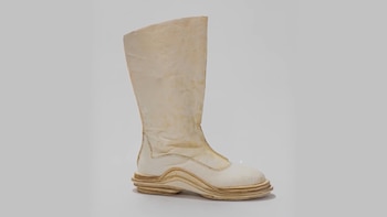 Bota de caña alta en tono blanco crema con textura arrugada y suela gruesa de varias capas onduladas en color madera claro sobre fondo gris claro